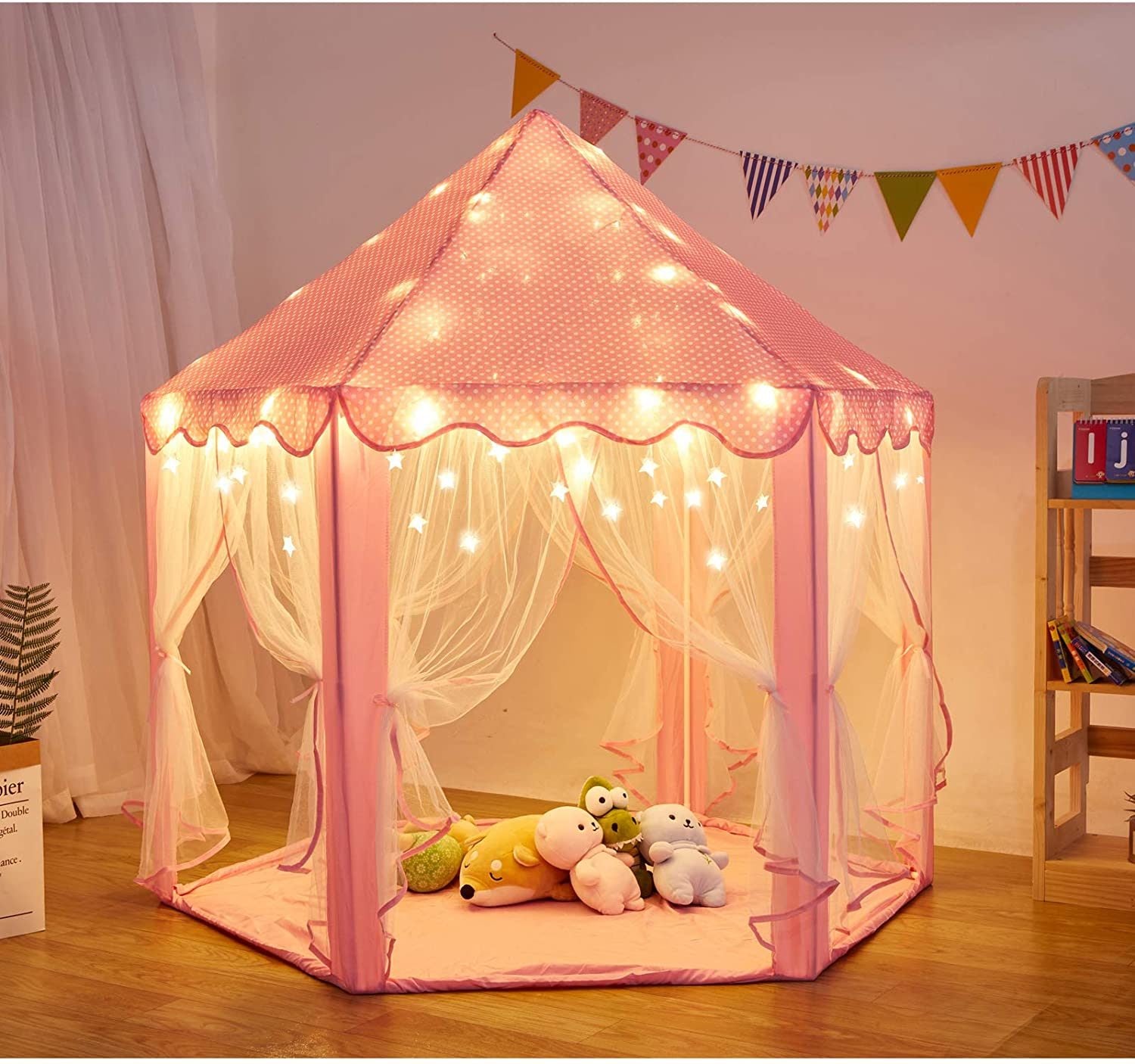 A pink Outdoor Indoor Portable Folding Princess Castle Tent Kids Children Funny Play Fairy House Kids Play Tent with its flap open, displaying several teddy bears inside, illuminated by string lights, with a star-shaped light visible at the top corner.