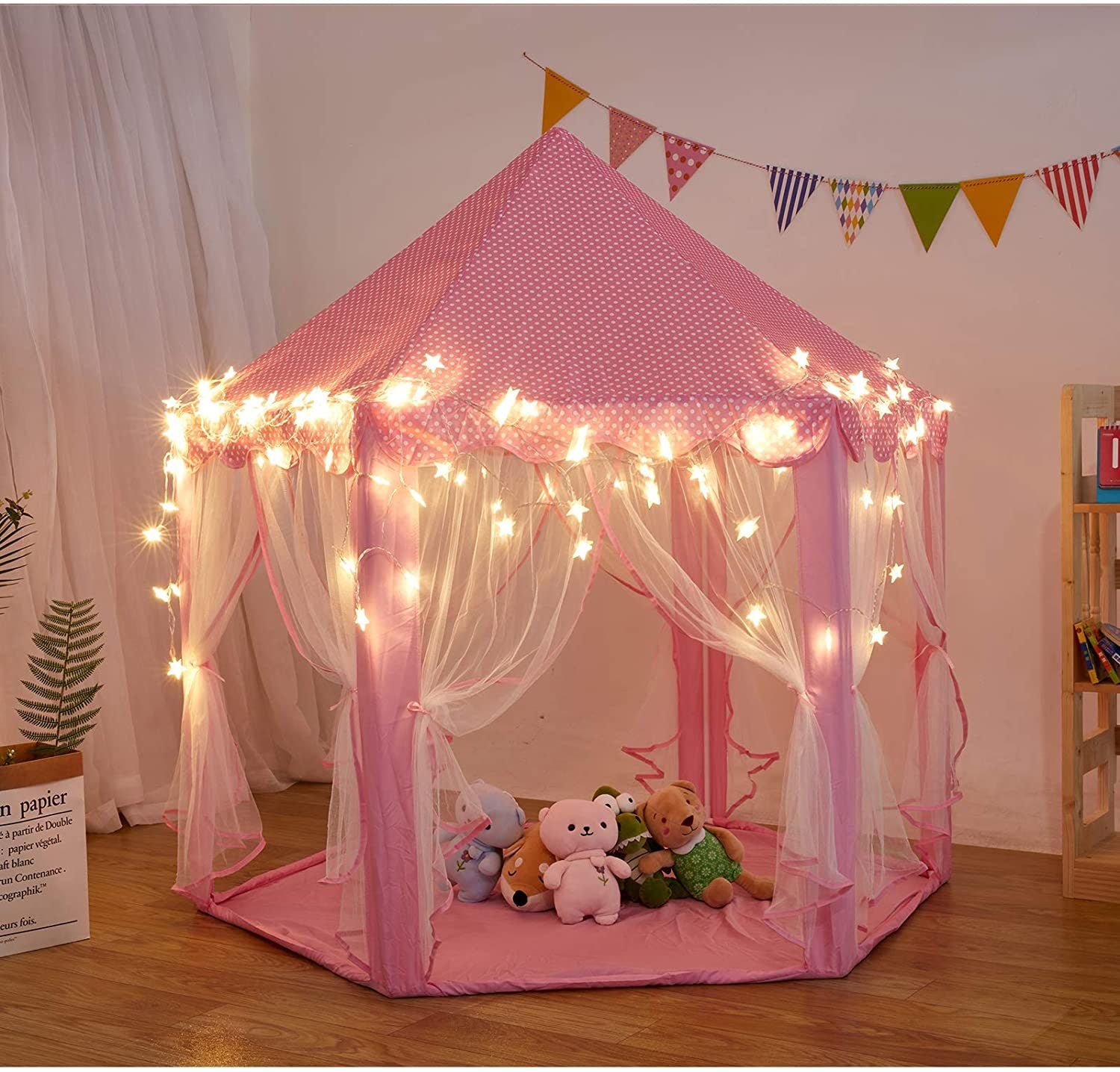 A pink Outdoor Indoor Portable Folding Princess Castle Tent Kids Children Funny Play Fairy House Kids Play Tent with its flap open, displaying several teddy bears inside, illuminated by string lights, with a star-shaped light visible at the top corner.