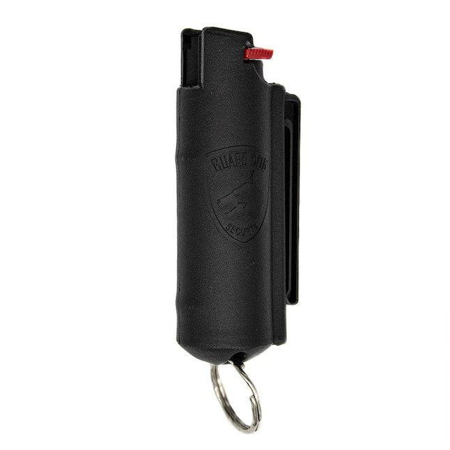 Guard Dog Pepper Spray keychain with integrated remote on a wooden table near a folded umbrella and a smartphone displaying text.