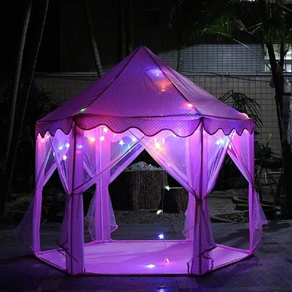 A purple children's Outdoor Indoor Portable Folding Princess Castle Tent Kids Children Funny Play Fairy House Kids Play Tent(LED Star Lights) illuminated by fairy lights at night, set up outdoors near a building.