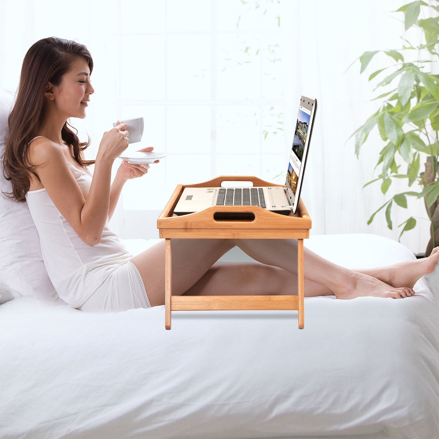Bamboo Folding Bed Table Breakfast Tray with legs, holding a cup, fruits, a jar of nuts, and a plate with cheese and crackers, on a white background.