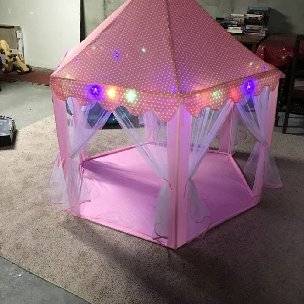 A purple children's Outdoor Indoor Portable Folding Princess Castle Tent Kids Children Funny Play Fairy House Kids Play Tent(LED Star Lights) illuminated by fairy lights at night, set up outdoors near a building.