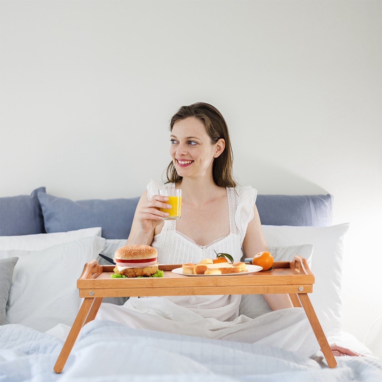 Bamboo Folding Bed Table Breakfast Tray with legs, holding a cup, fruits, a jar of nuts, and a plate with cheese and crackers, on a white background.