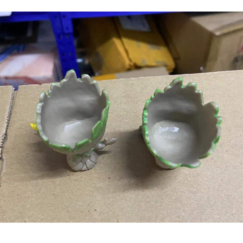 A Guardians of the Galaxy Groot Tree Man Hand Ornament, crafted from PVC, holding a small bird, with green leaves sprouting from its head, isolated on a white background.