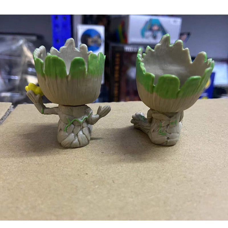 A Guardians of the Galaxy Groot Tree Man Hand Ornament, crafted from PVC, holding a small bird, with green leaves sprouting from its head, isolated on a white background.