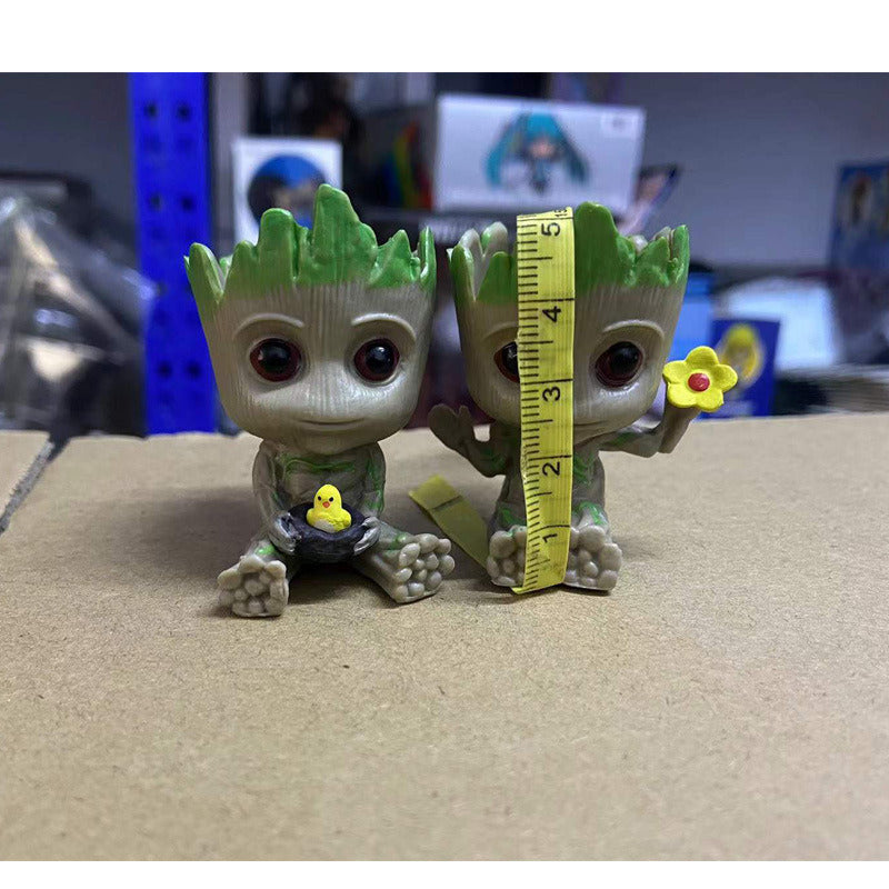 A Guardians of the Galaxy Groot Tree Man Hand Ornament, crafted from PVC, holding a small bird, with green leaves sprouting from its head, isolated on a white background.