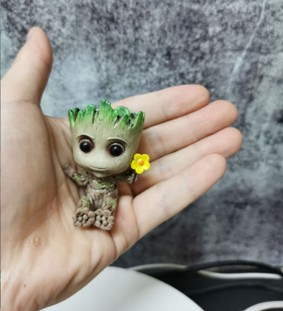 A Guardians of the Galaxy Groot Tree Man Hand Ornament, crafted from PVC, holding a small bird, with green leaves sprouting from its head, isolated on a white background.
