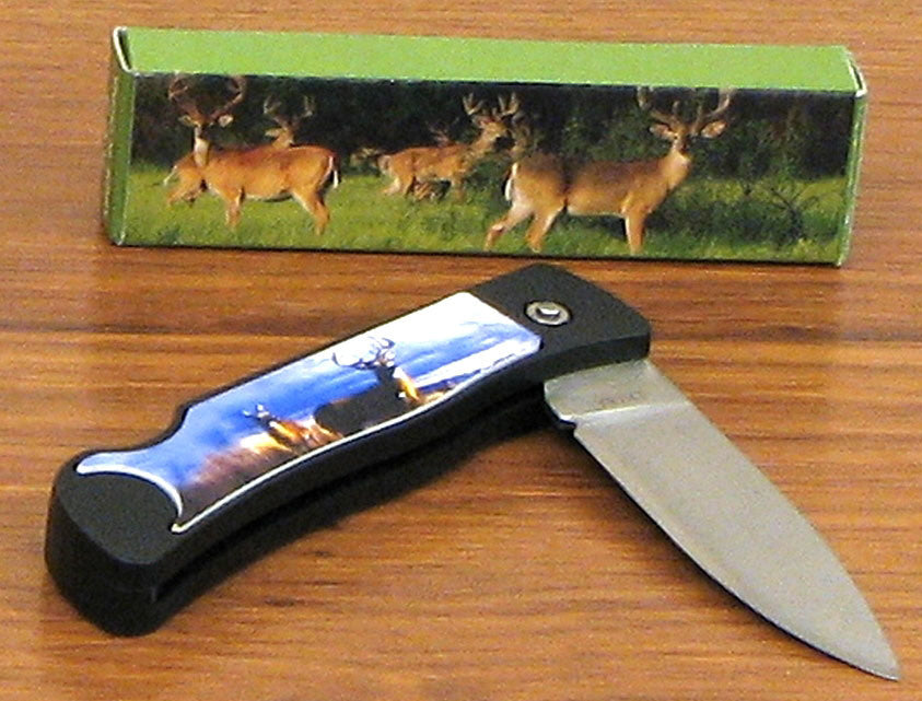 A Deer Scene Knife w/Lock Blade with a scenic wildlife illustration on its handle, displayed in front of its packaging featuring deer.