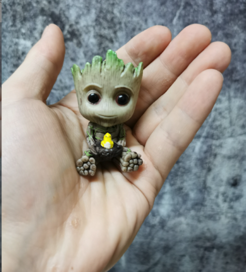 A Guardians of the Galaxy Groot Tree Man Hand Ornament, crafted from PVC, holding a small bird, with green leaves sprouting from its head, isolated on a white background.
