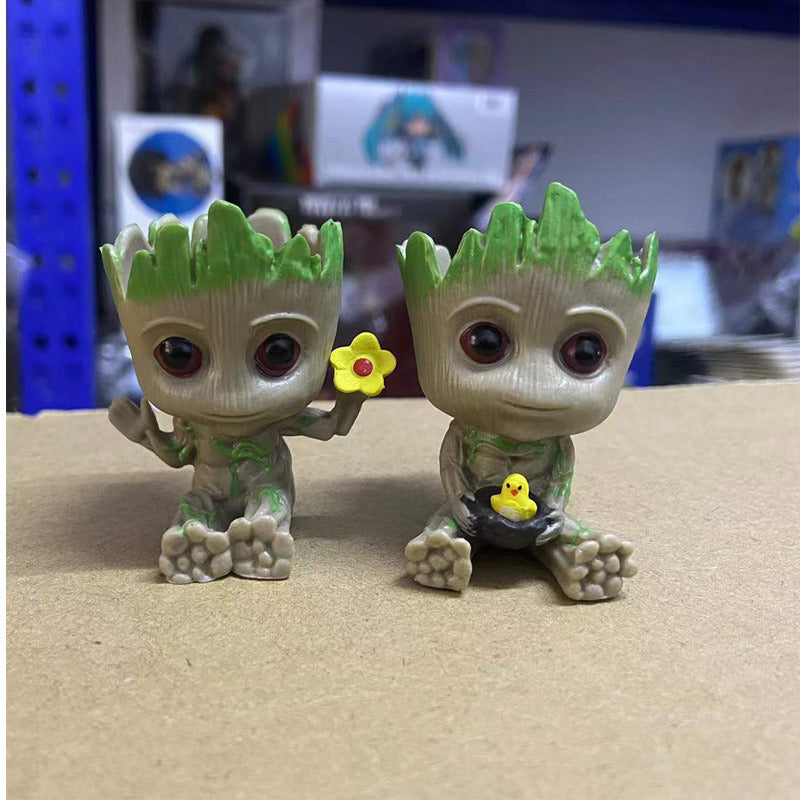 A Guardians of the Galaxy Groot Tree Man Hand Ornament, crafted from PVC, holding a small bird, with green leaves sprouting from its head, isolated on a white background.