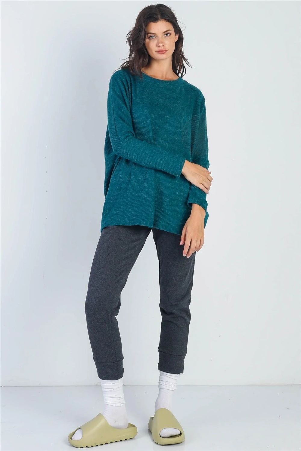 A person stands in front of a plain background wearing the Cherish Apparel Round Neck Long Sleeve Sweater in teal, dark gray pants, white socks, and beige slide sandals—a classic wardrobe staple.