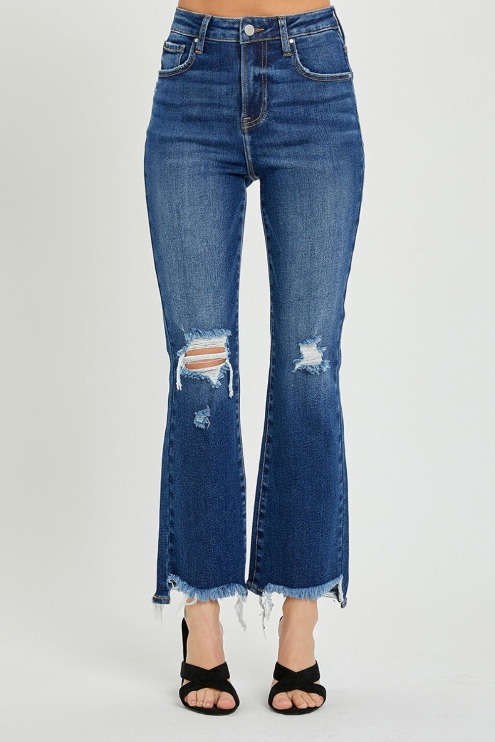 A person wearing RISEN High Rise Distressed Crop Flare Jeans with frayed hems stands with their right hand on their left hip, paired with black open-toed sandals.