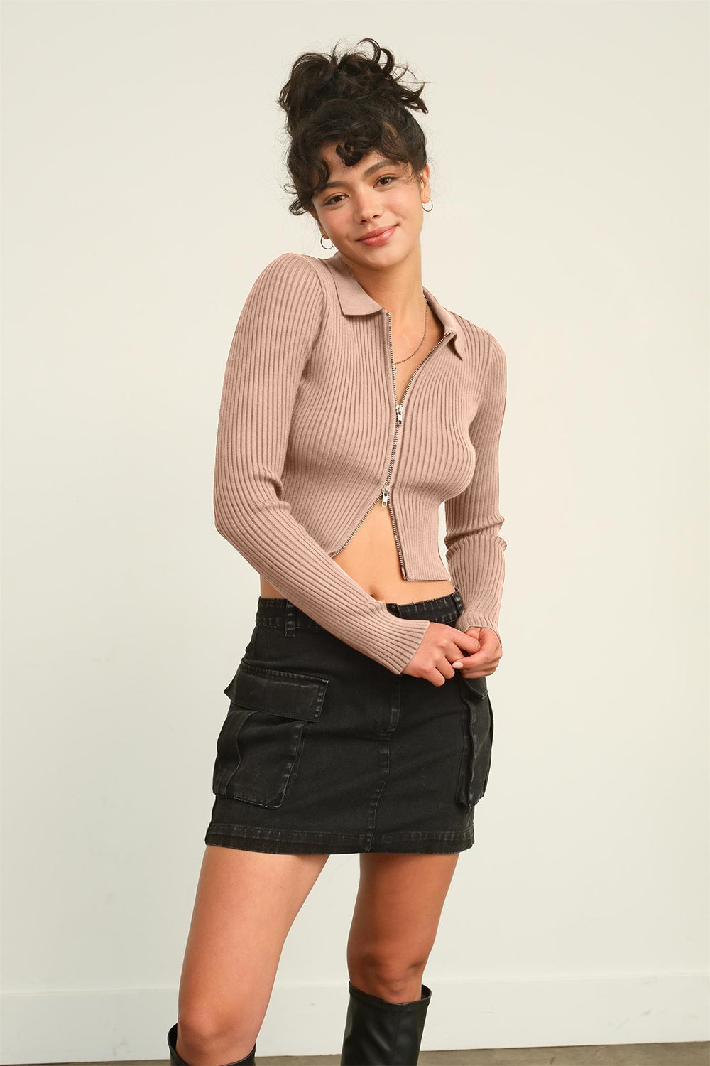 A woman in a HYFVE Ribbed Double Zip Cropped Cardigan and a black skirt poses gracefully against a plain background.