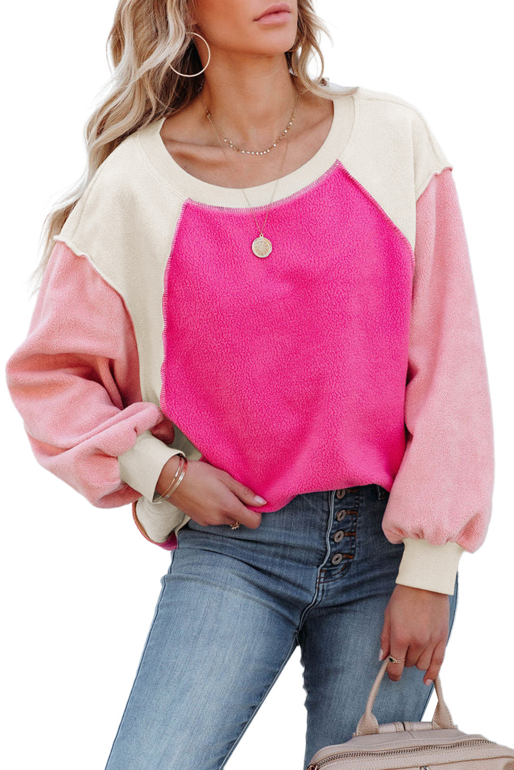 A person with long blonde hair is standing facing away from the camera against a beige background, showcasing the comfortable fleece fabric of the Rose Colorblock Long Sleeve Pullover Fleece Sweatshirt in pink shades and light blue jeans.