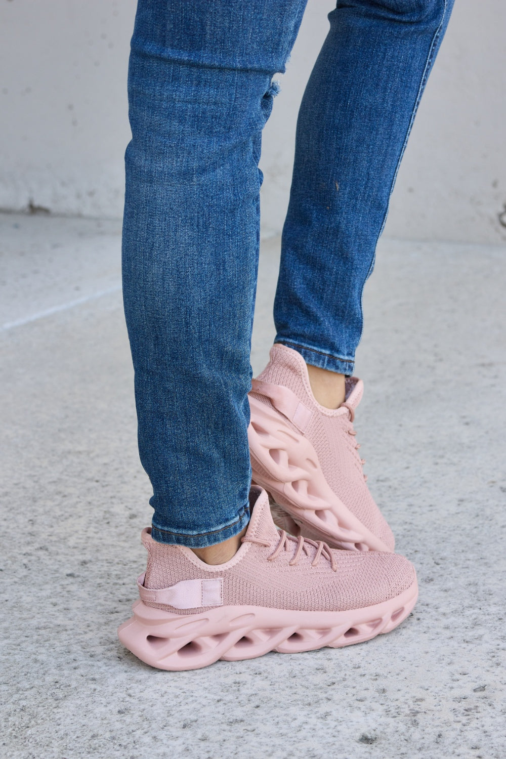 Person wearing blue ripped jeans and Forever Link Mesh Breathable Platform Athletic Shoes in light pink, standing on a concrete surface.