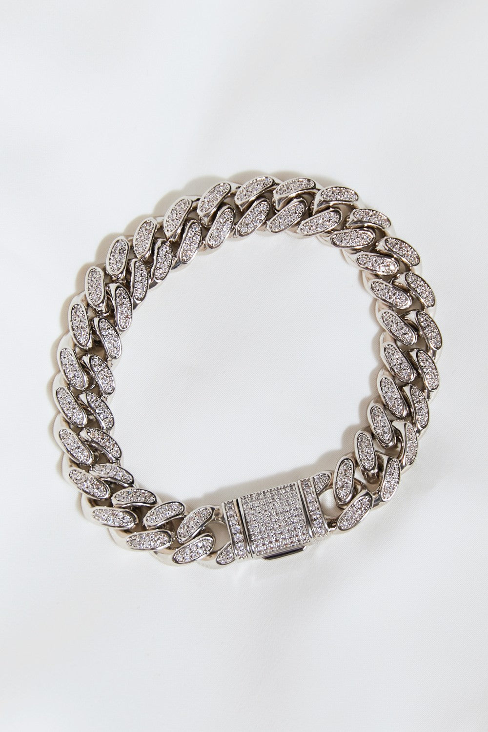 The Curb Chain Bracelet, crafted from silver and adorned with sparkling diamonds, elegantly graces the wrist against a white background.