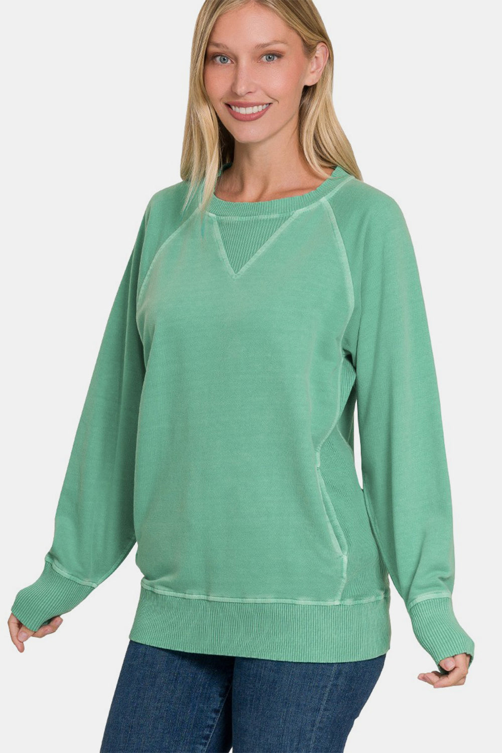 A person wearing a Zenana Pocketed Round Neck Long Sleeve Sweatshirt in green and jeans, smiling against a plain background.