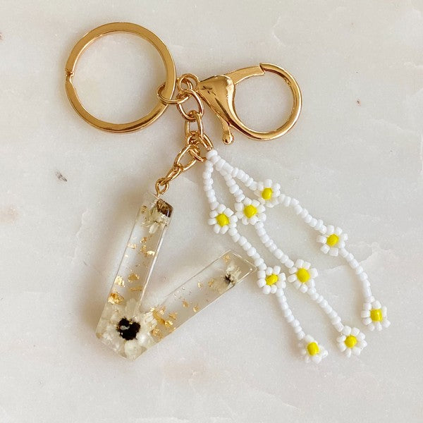 Baby Daisy Initial Key Chain alphabet keychains with real daisy flowers and gold flakes on a marble surface.