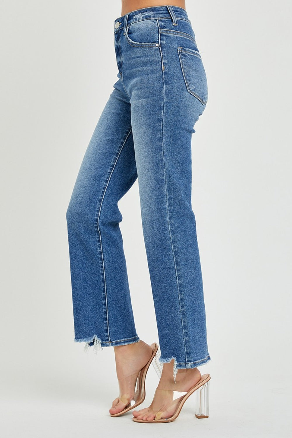 Person wearing RISEN High Rise Straight Jeans with frayed hem and clear-strap heels, standing against a plain background, showcasing a classic silhouette.