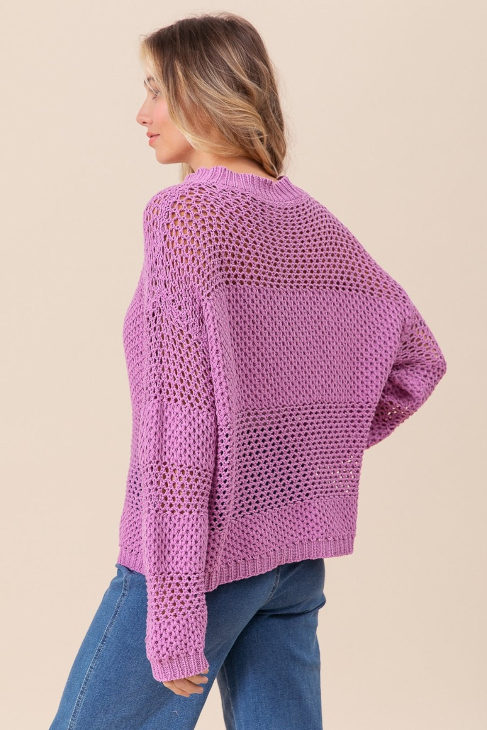 Wearing the BiBi Openwork Long Sleeve Knit Top in purple and blue jeans, a person smiles slightly while gazing to the side, exuding a fashion-forward vibe.