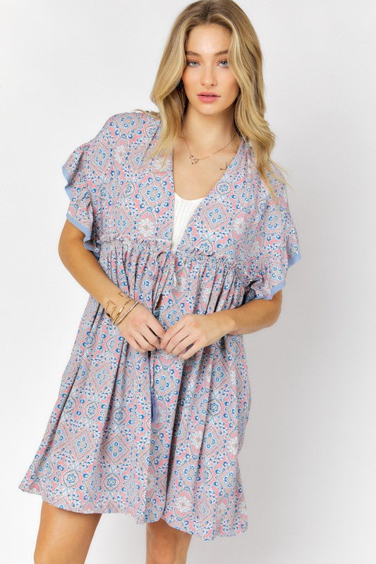 A woman stands against a white background wearing the Printed Short Sleeve Ruffle Kimono over a white top and denim shorts, effortlessly blending style and comfort.