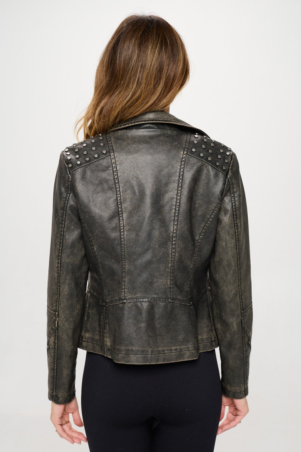 A person wearing the Coalition LA Studded Classic Moto Faux Leather Jacket, along with a black crop top and black pants, stands against a white background.