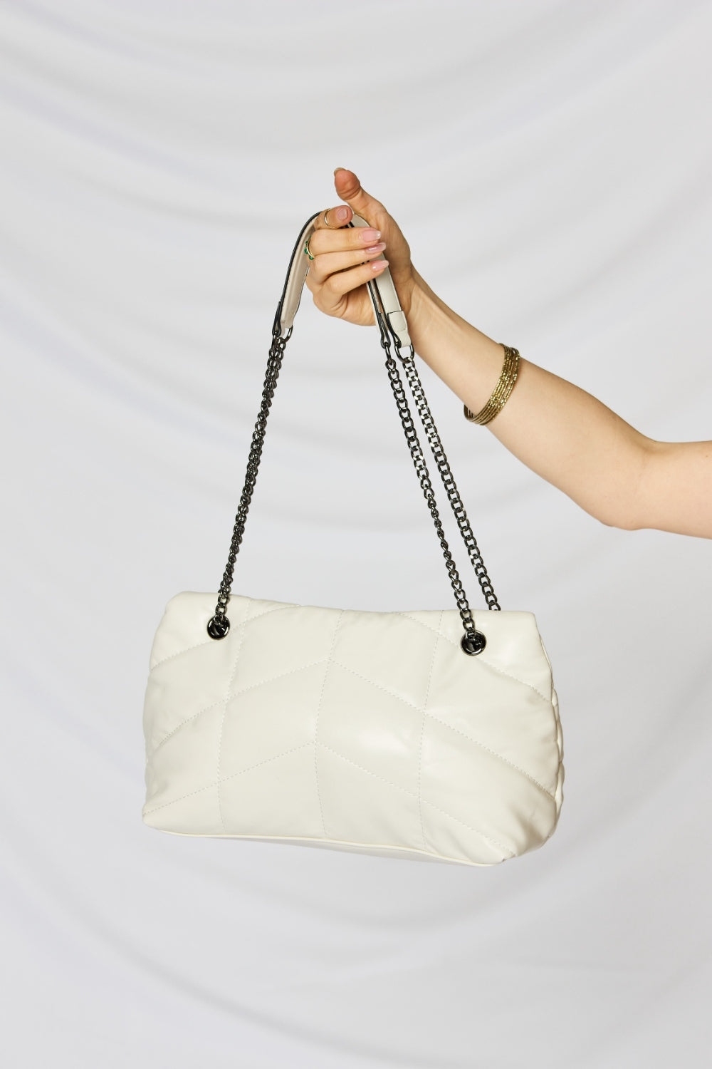 A person holding a stylish SHOMICO PU Leather Chain Handbag over their shoulder against a white background. They are dressed in a beige outfit and looking at the camera, embodying sustainable fashion.