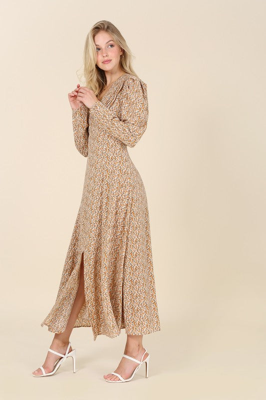 A woman gracefully poses against a beige background wearing the Fit and Flare floral maxi dress, featuring a V-neckline, elegant puff sleeves, and a complementary front slit.