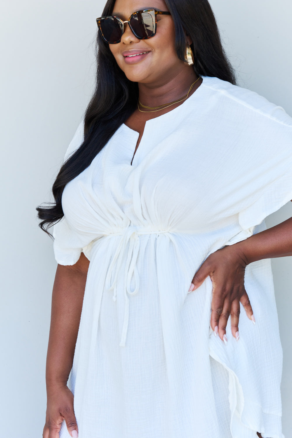 A person with long dark hair smiles while posing in the Ninexis Out Of Time Full Size Ruffle Hem Dress with Drawstring Waistband in White against a plain background.