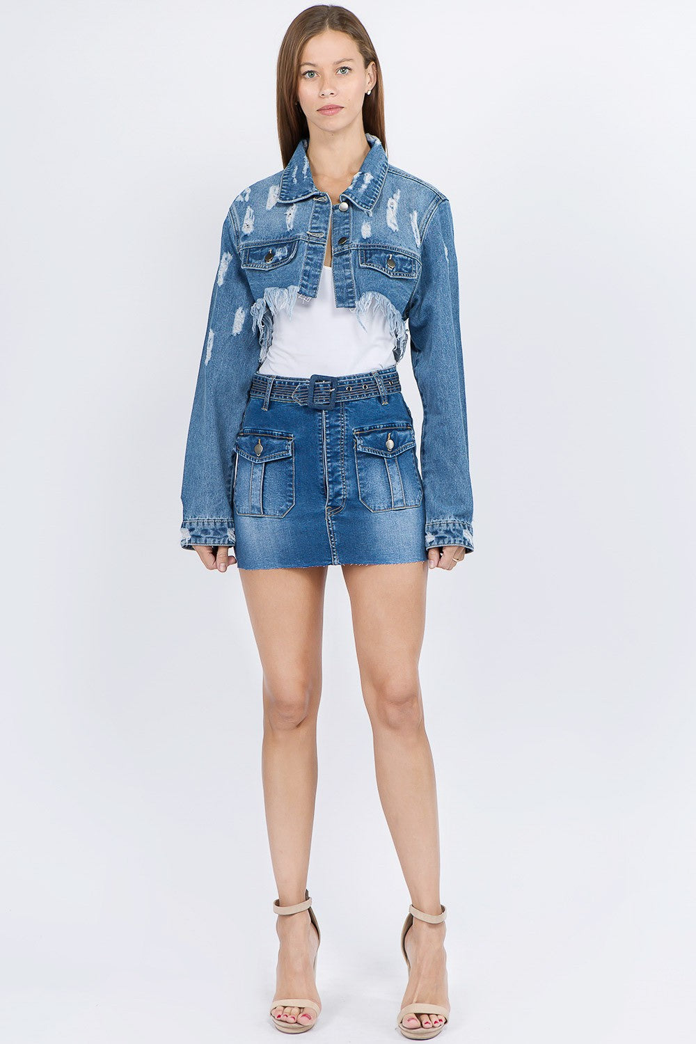 A woman wearing an American Bazi Distressed Denim Jacket with a frayed hem and matching skirt poses against a plain background.