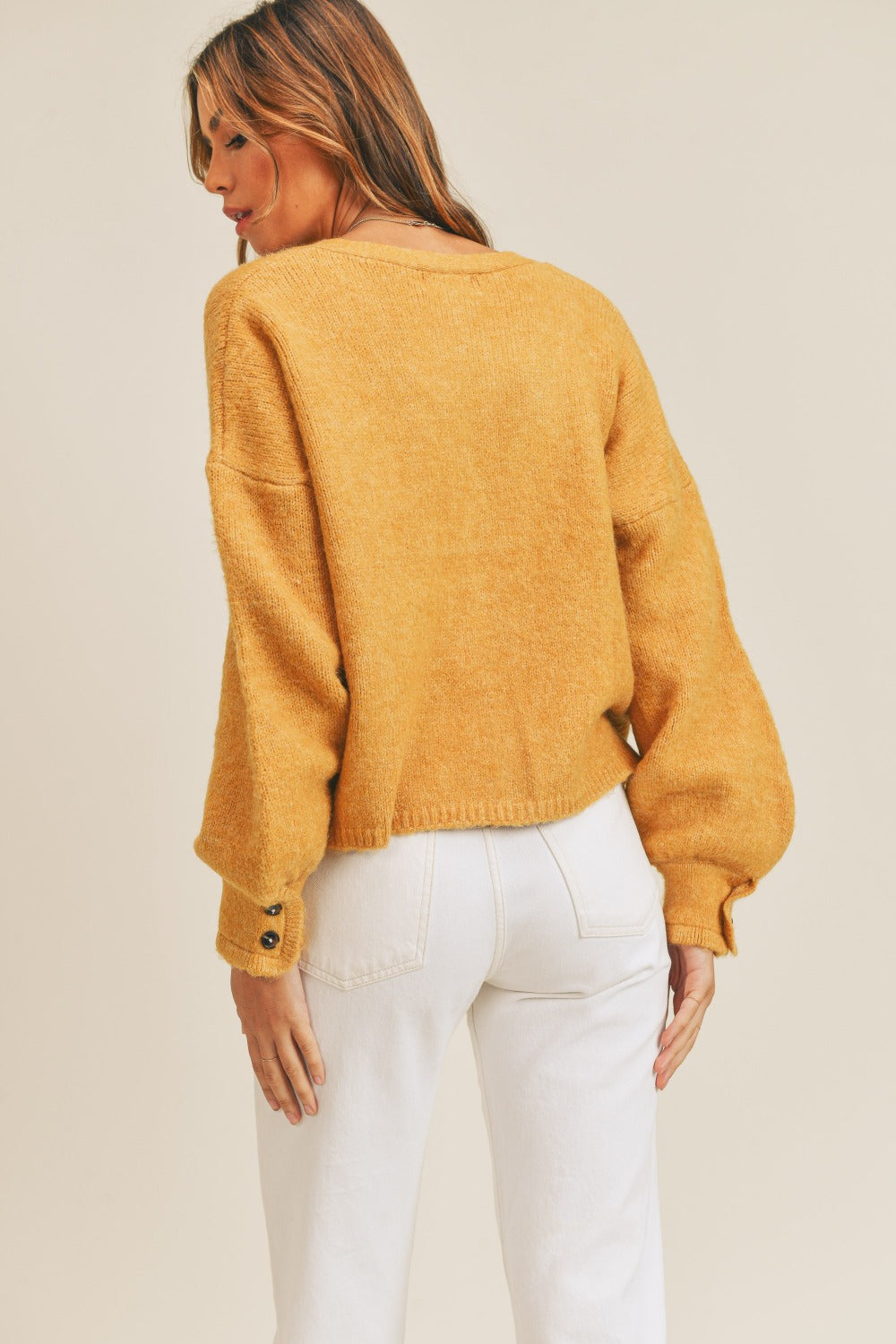 A person wears the MABLE Long Sleeve Button Down Sweater Cardigan in mustard, paired with white high-waisted pants, standing in front of a plain background.