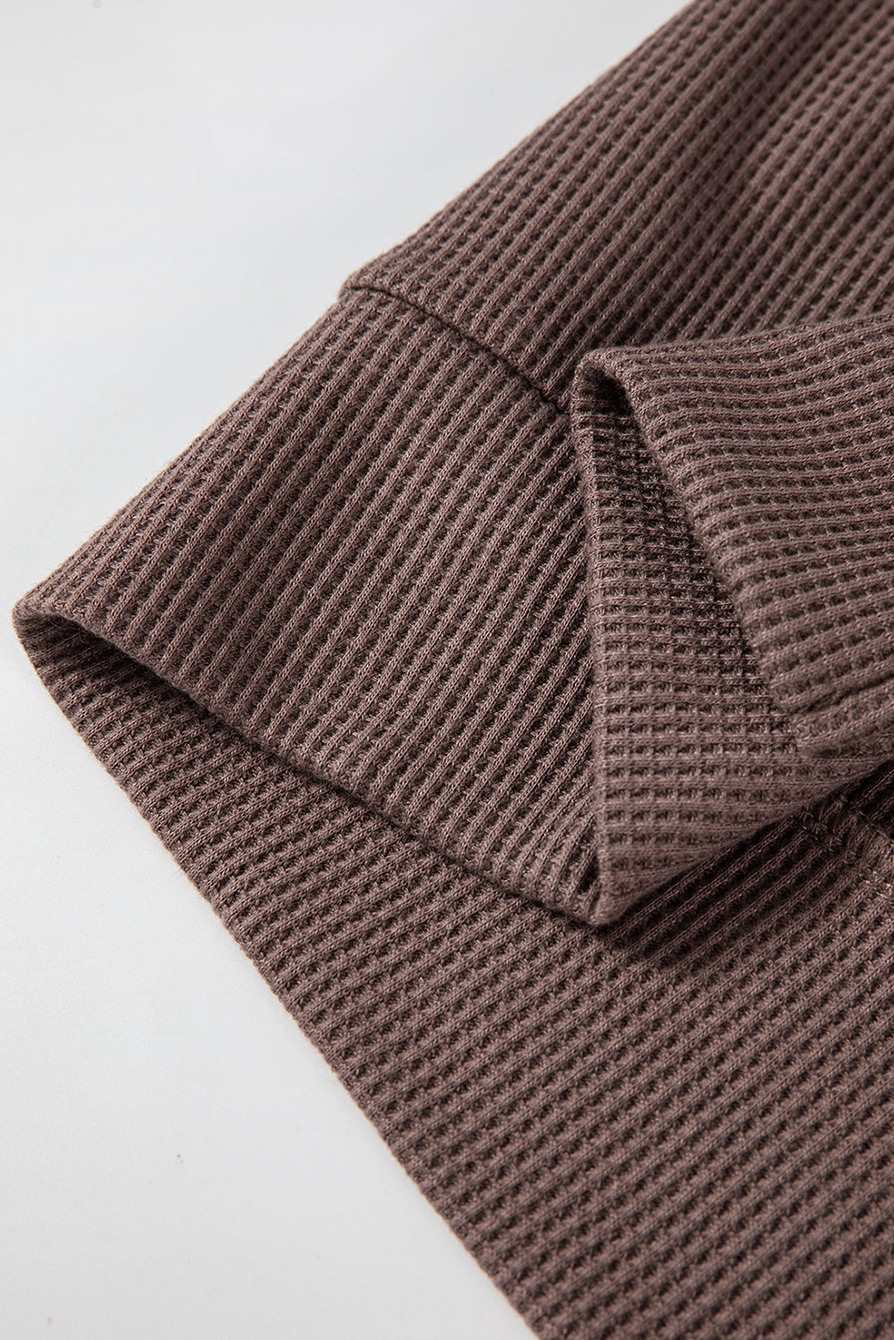 A woman with long hair is standing in profile, wearing a Coffee Waffle Knit Fleece Lined High Low Oversized Hoodie and black shorts. The background is a plain light gray.