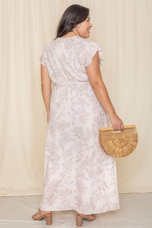 A woman wearing a Floral Surplice Sash Sundress, which is light yellow and unlined, stands smiling against a cream-colored background.