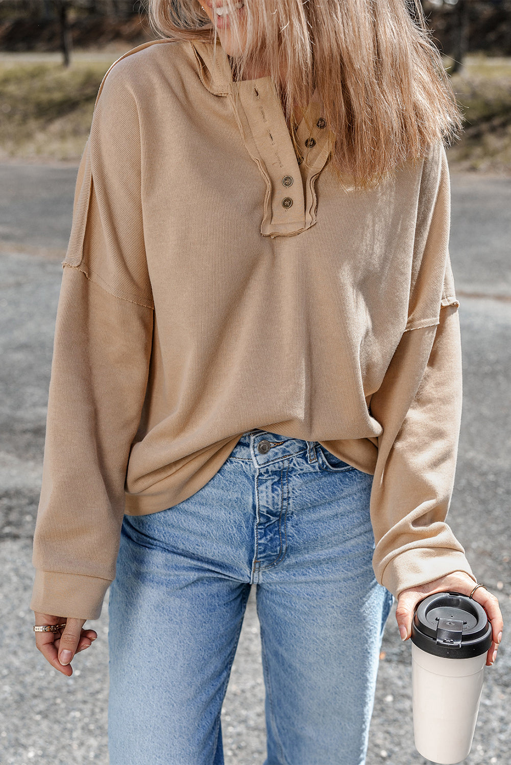 Person wearing a Khaki Casual Button Solid Patchwork Trim Hoodie and blue jeans is standing outdoors holding a white tumbler. The individual's blonde hair is partially visible from behind.