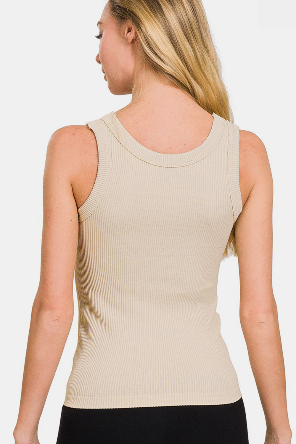 A person with long hair wears the Zenana 2 Way Neckline Washed Ribbed Tank—a beige, essential versatile wardrobe piece—paired with black pants, smiling slightly against a plain white background.