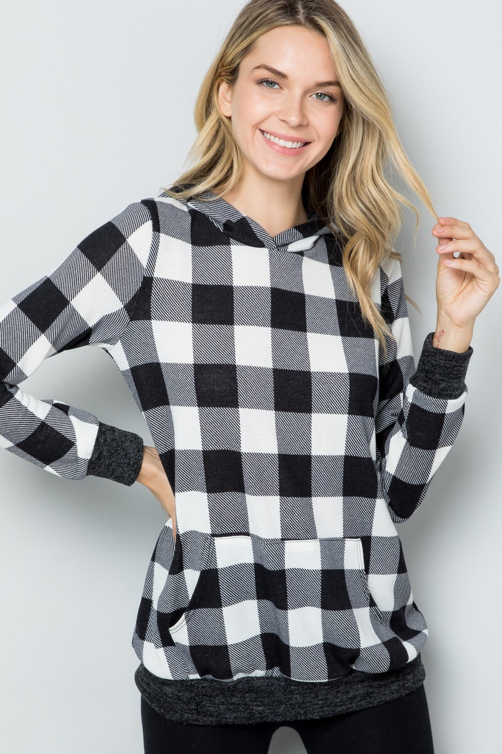 A woman wearing the Celeste Full Size Contrast Plaid Long Sleeve Hoodie smiles while standing against a plain background, showcasing her casual wardrobe.