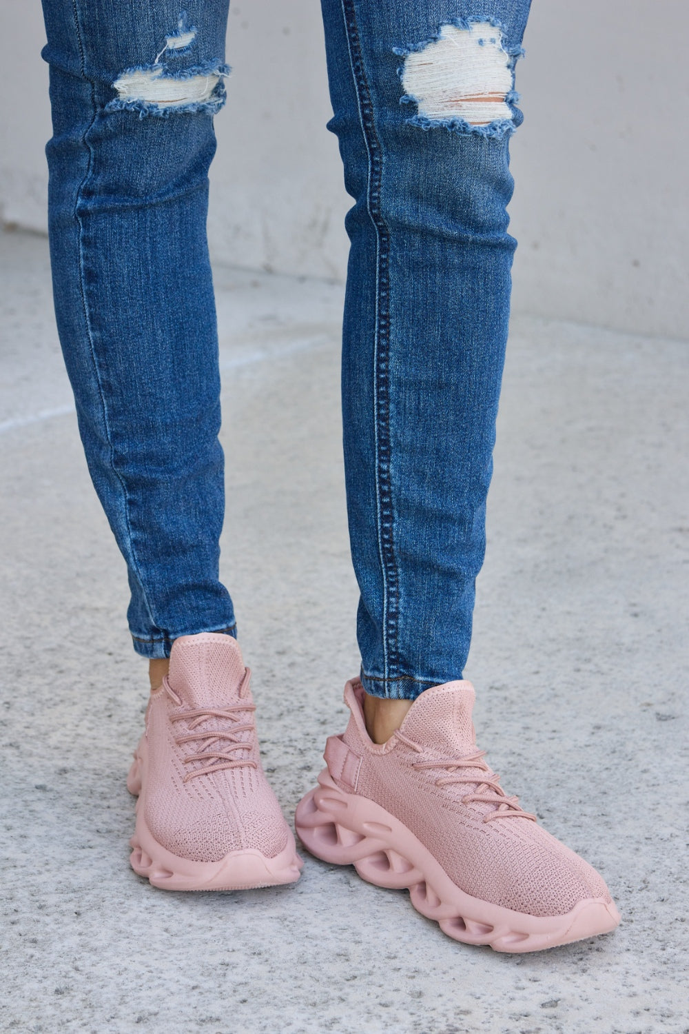 Person wearing blue ripped jeans and Forever Link Mesh Breathable Platform Athletic Shoes in light pink, standing on a concrete surface.