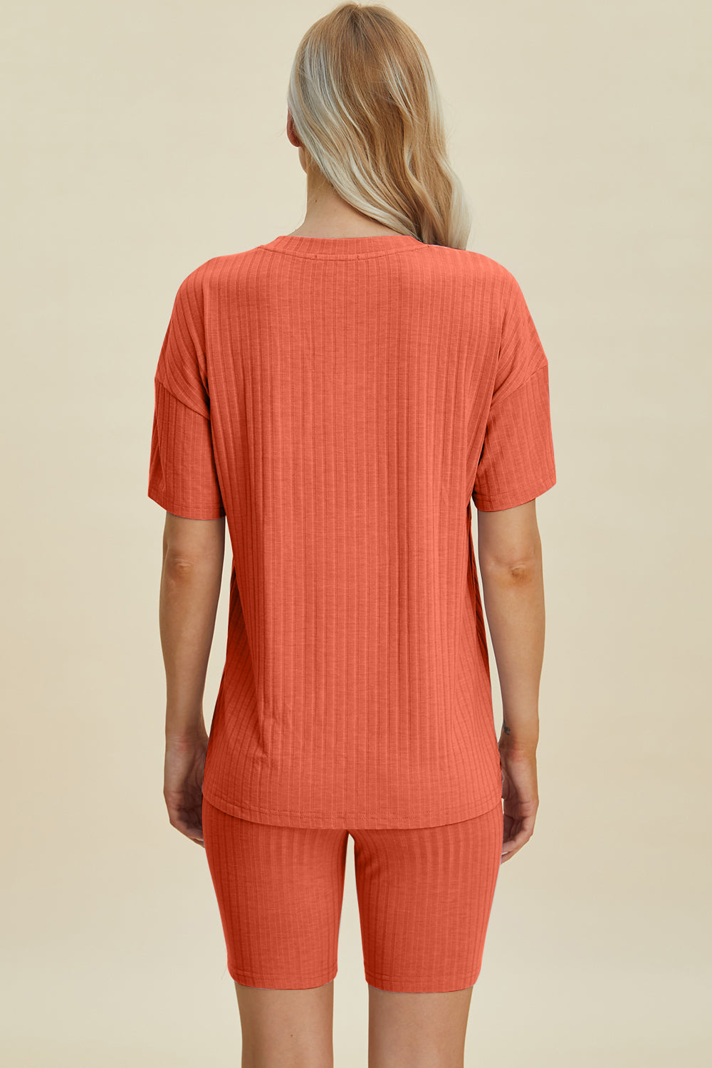 A woman with long blonde hair wearing the Basic Bae Full Size Ribbed V-Neck Short Sleeve Top and Shorts Set in rust stands against a plain background. This stylish two-piece set is made from a comfortable, stretchy fabric that is also machine washable.