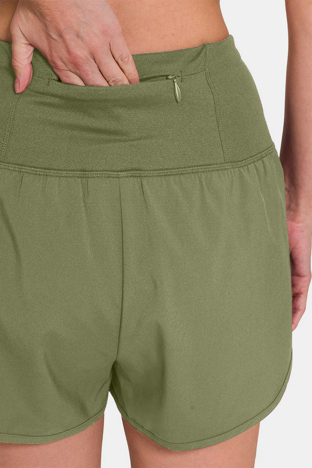 Individual sporting Zenana High-Waisted Zippered Back Pocket Active Shorts in light green, featuring a wide waistband, side slits, and a convenient zippered back pocket—ideal for active wear.