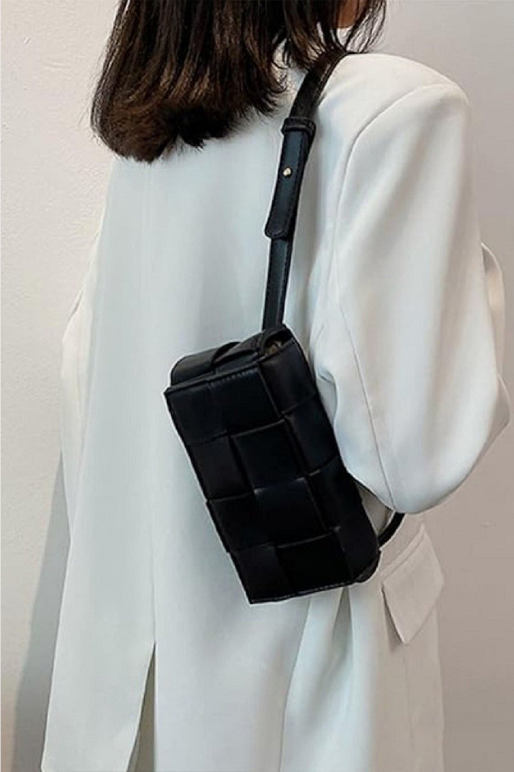 Person wearing a white button-up shirt and holding a black Zenana Vegan Leather Woven Crossbody Bag.