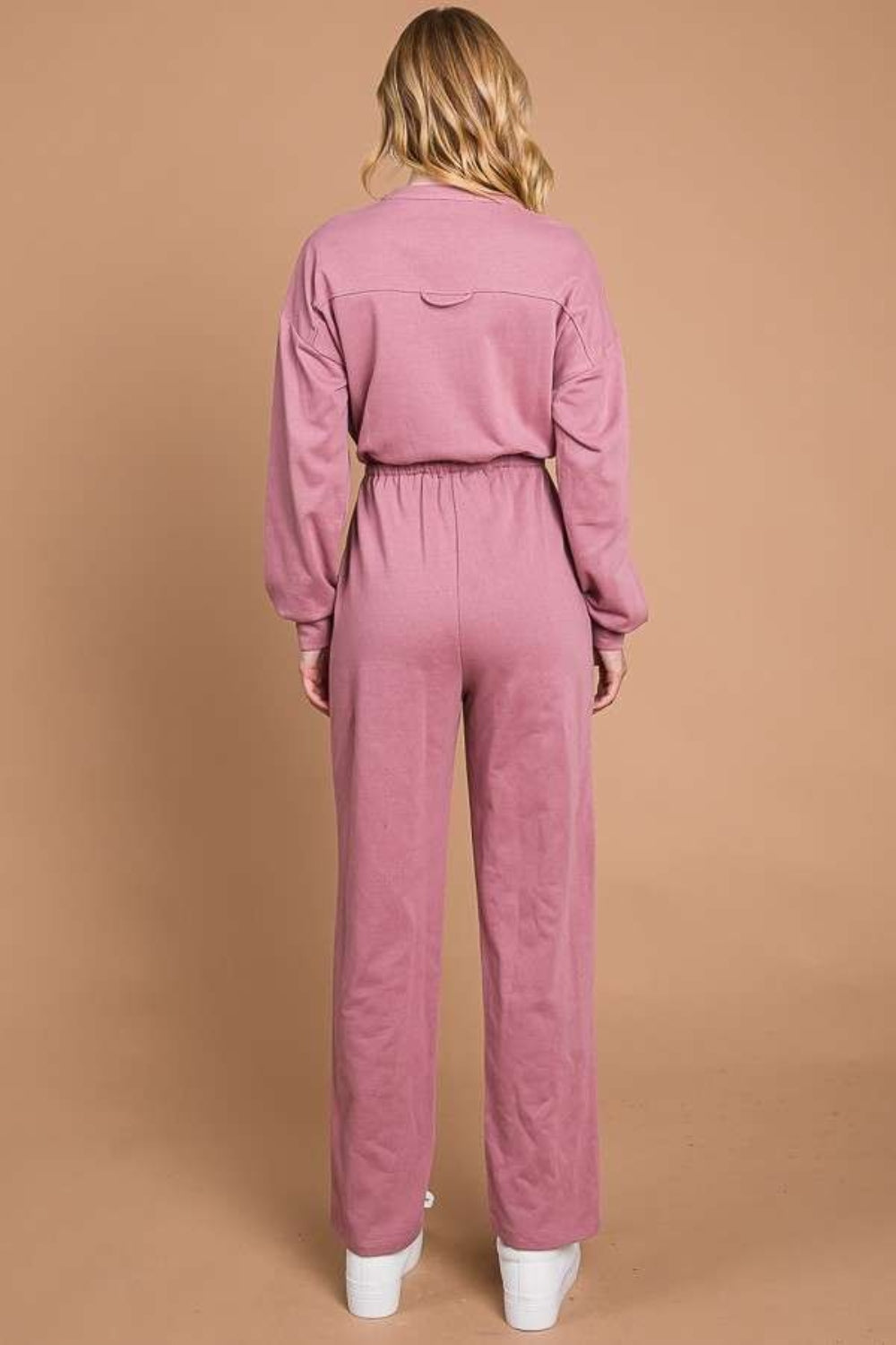 Against a beige background, an individual models the Culture Code Full Size Button Up Drawstring Waist Straight Jumpsuit, which features a stylish pink design with pockets and a chic drawstring waist.