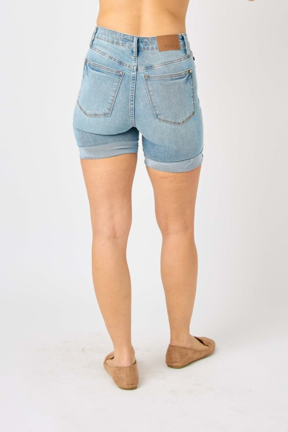 Person wearing Judy Blue Full Size Tummy Control Denim Shorts, which have a flattering fit, paired with brown shoes against a plain white background.