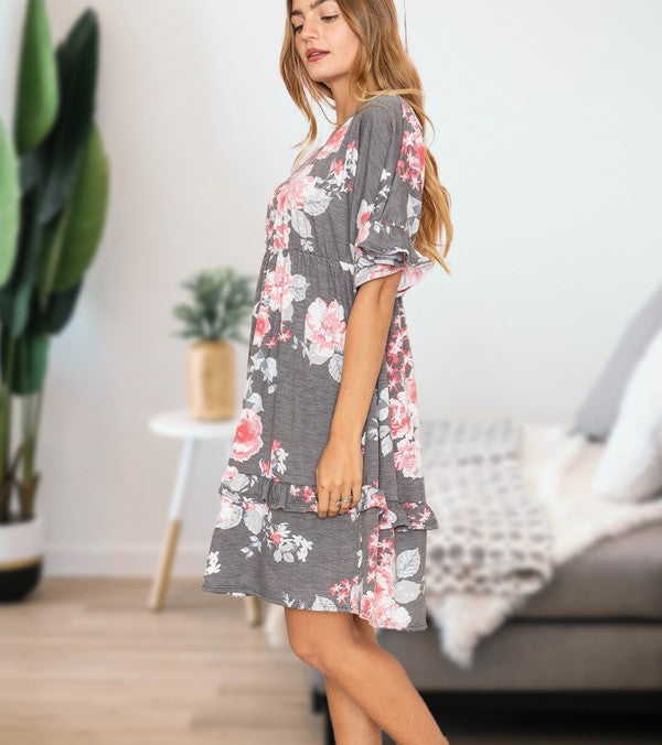 A woman wearing a Floral V Neck Ruffle Dress holds a wicker handbag, standing in a room decorated with a plant and partially visible furniture in the background.