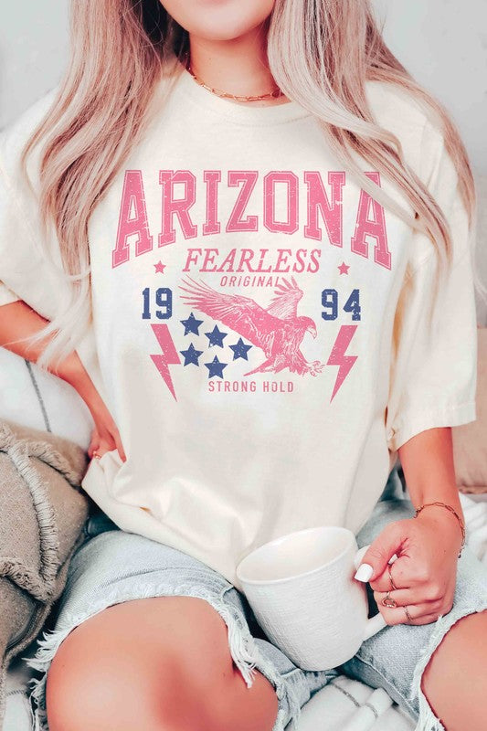 A woman with long light hair is wearing jeans and a 100% cotton ARIZONA EAGLE 1994 Graphic Tee, which features the text "ARIZONA FEARLESS ORIGINAL 1994 STRONG HOLD" along with an eagle, stars, and lightning bolts.