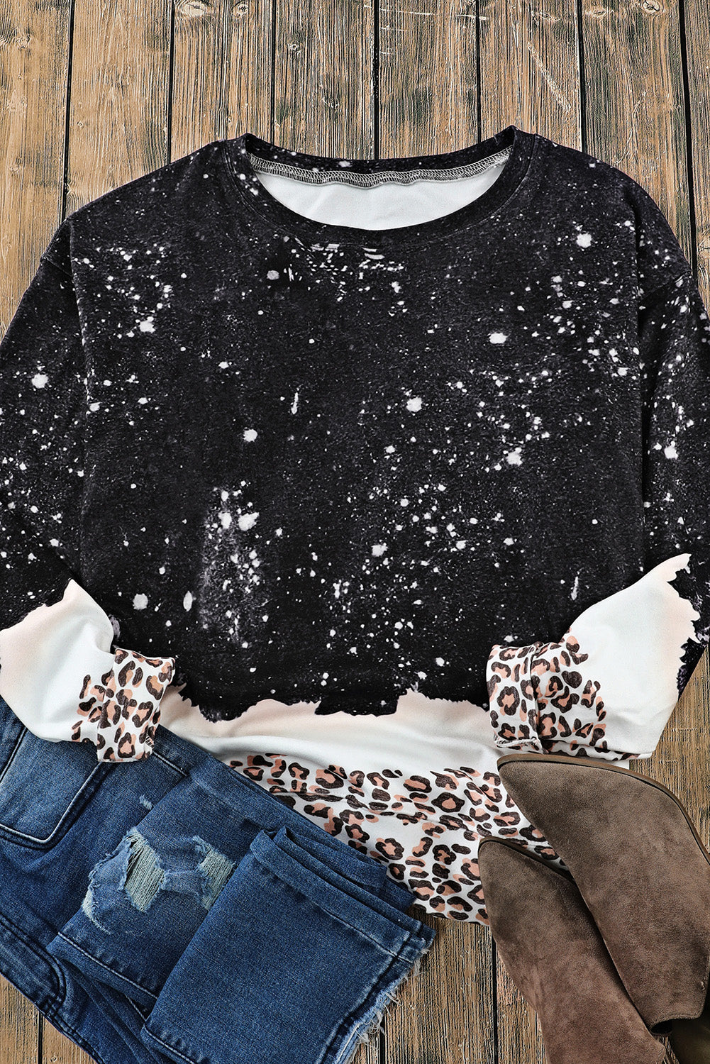 A Black Leopard Bleached Pullover Sweatshirt is laid out with distressed blue jeans and brown suede ankle boots on a wooden surface.