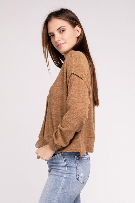 A woman in a pink Brushed Melange Hacci Hi-Low Hem Sweater and blue jeans standing with her hands clasped, against a gray background.
