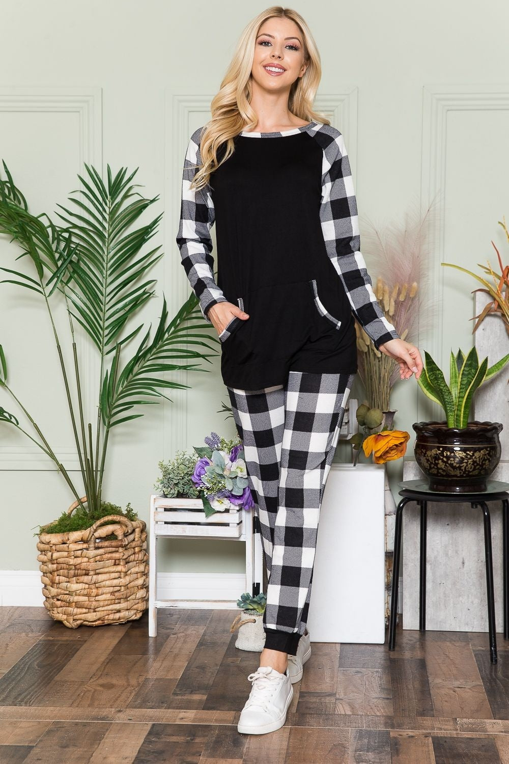 A person wearing the Celeste Plaid Long Sleeve T-Shirt with Pockets stands in a room filled with plants and wooden flooring, presenting a laid-back style.