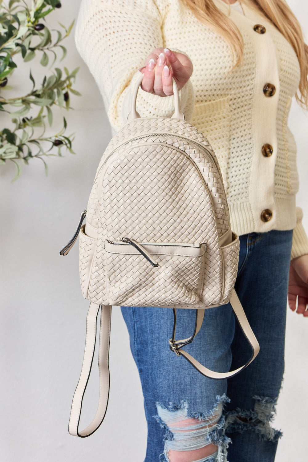 A person wearing a cream sweater and jeans is carrying the SHOMICO PU Leather Woven Backpack in brown.