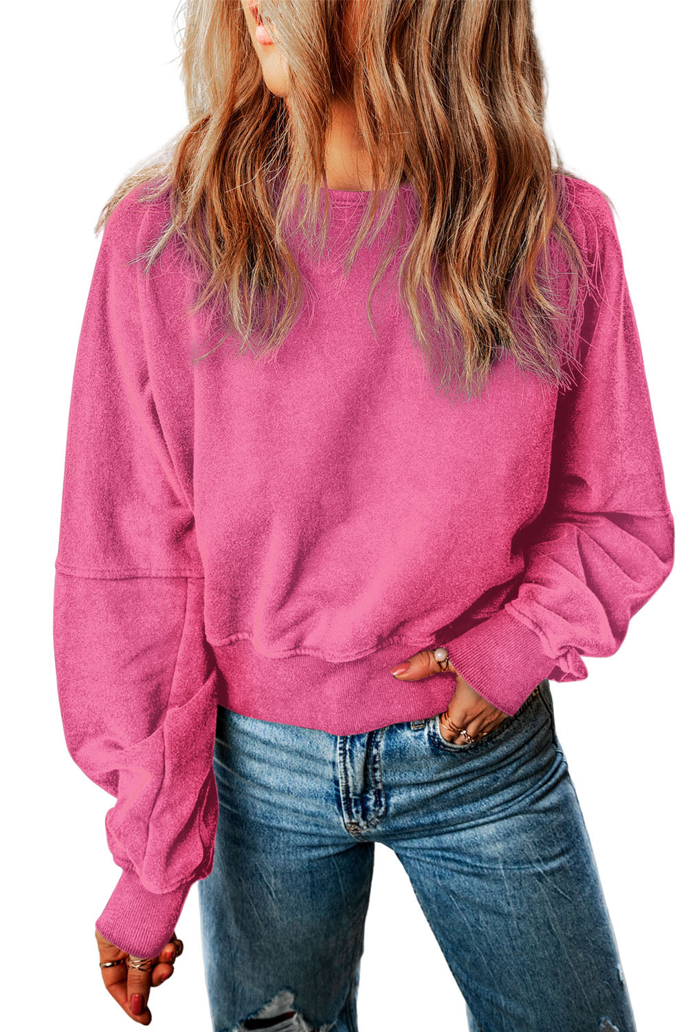 A person with wavy blonde hair is wearing a Rose Acid Wash V-shape Open Back Sweatshirt and blue jeans, walking on a paved path outdoors.