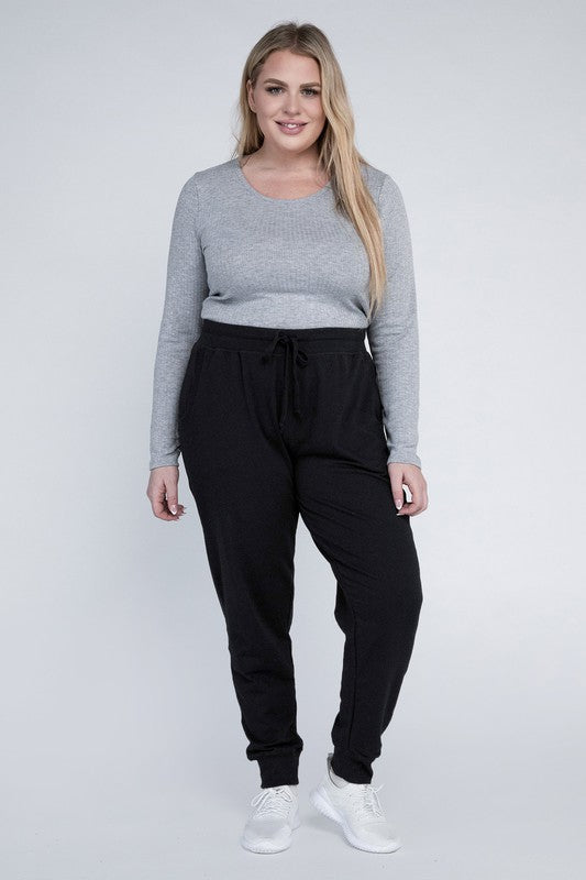 A person stands against a white background, wearing a white t-shirt, grey Plus-Size Jogger Pants with an adjustable waistband, and white sneakers. They have long blonde hair and are posing with one hand on their hip.